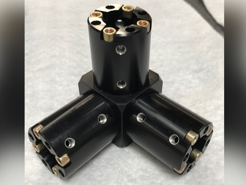 Black metallic CARBONNect™ corner section sitting on a surface before incorporation into the avionics workstation. The corner section is square with tubular connection structures projecting from three sides.